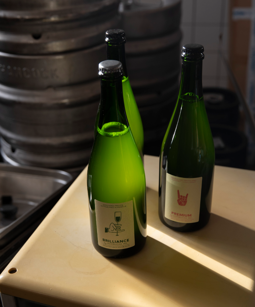 Two bottles from Kombucha Inc. beside steel kegs