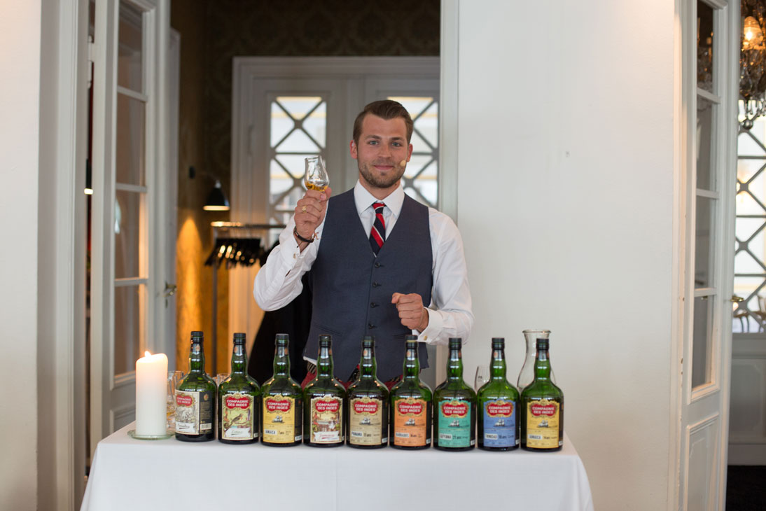 Man holding a tasting glass behind a row of Compagnie des Indes rum bottles